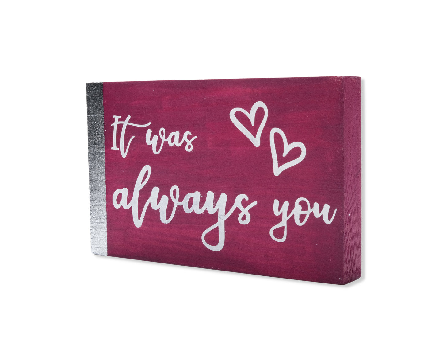 Small freestanding rectangular wooden sign displayed at 35 degree angle to show depth of sign. Magenta color, with silver vertical border on left side only. White painted message, It was always you, with two heart outlines in top right corner.