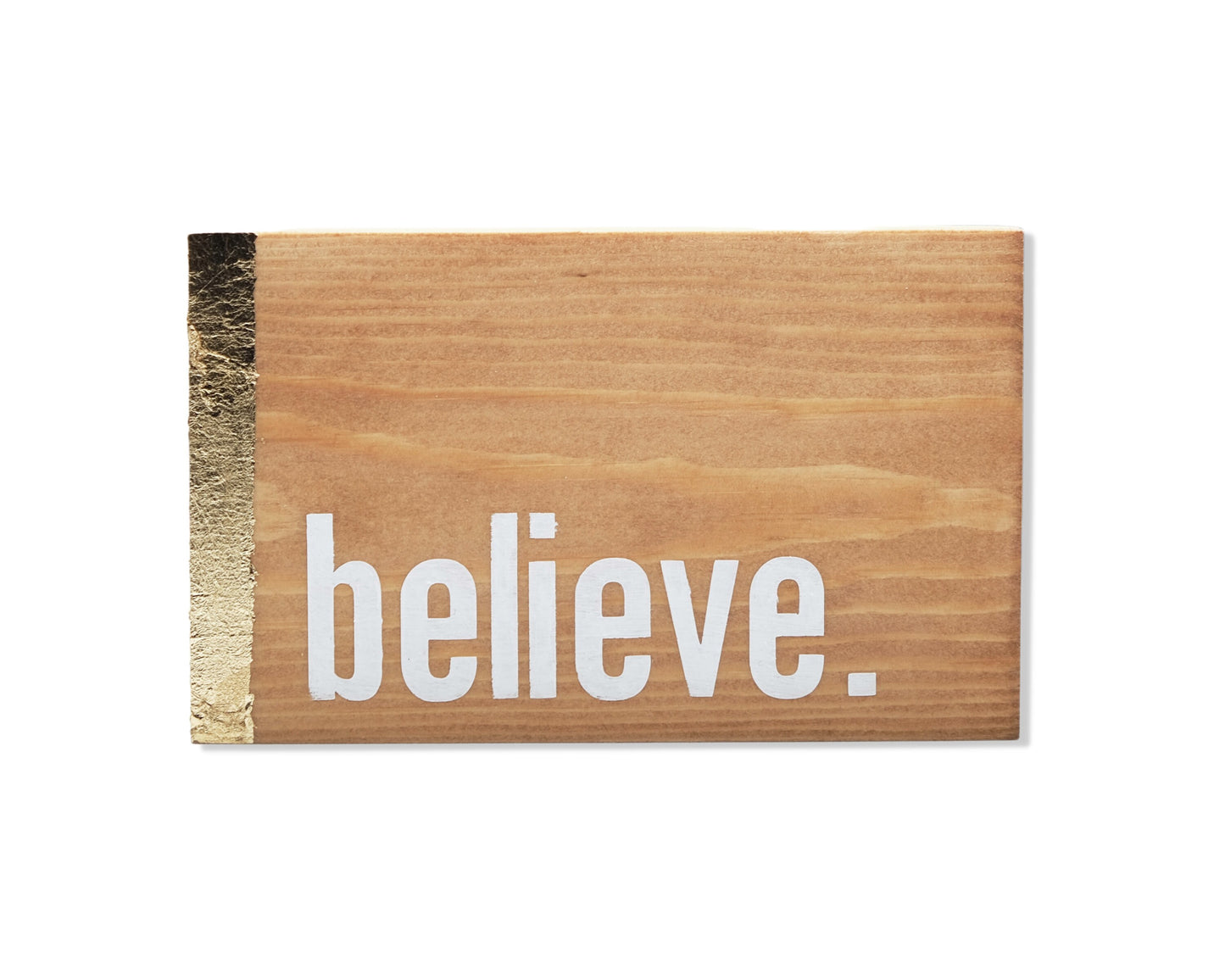 Small freestanding rectangular wooden sign facing straight on. Natural wood with gold vertical border on left side. White painted message in chunky font with full stop, believe. Studio style photo with white background.