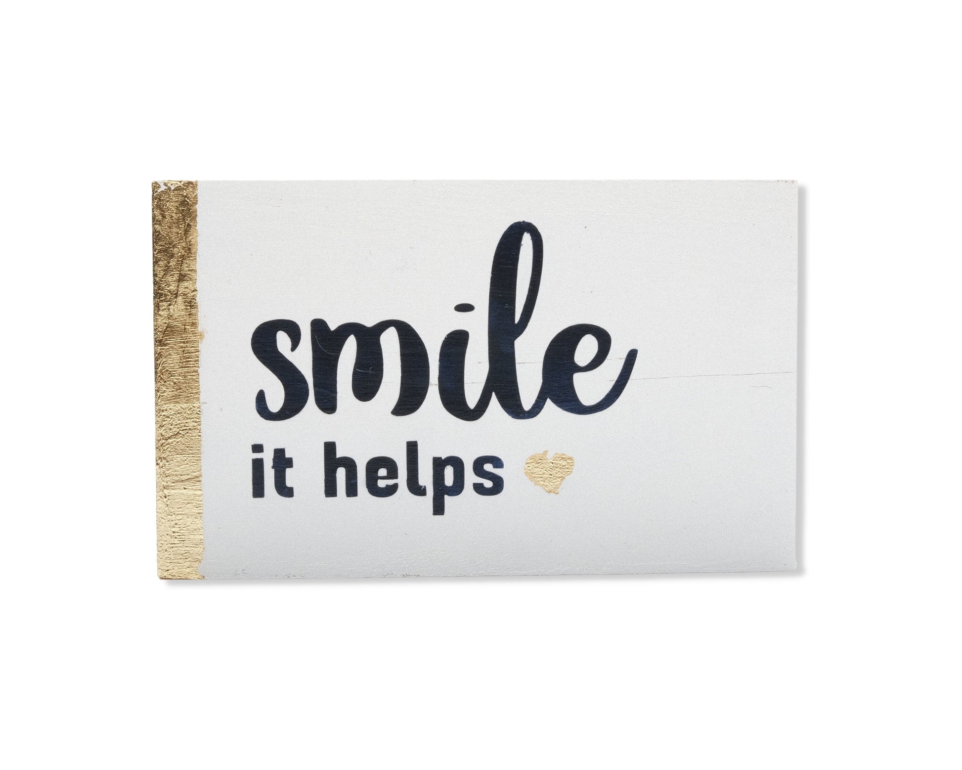 Small freestanding rectangular wooden sign facing straight on. White wood stain with gold vertical border on left side. Black painted message, smile it helps. Small solid heart in gold leaf foil. Studio style photo with white background.